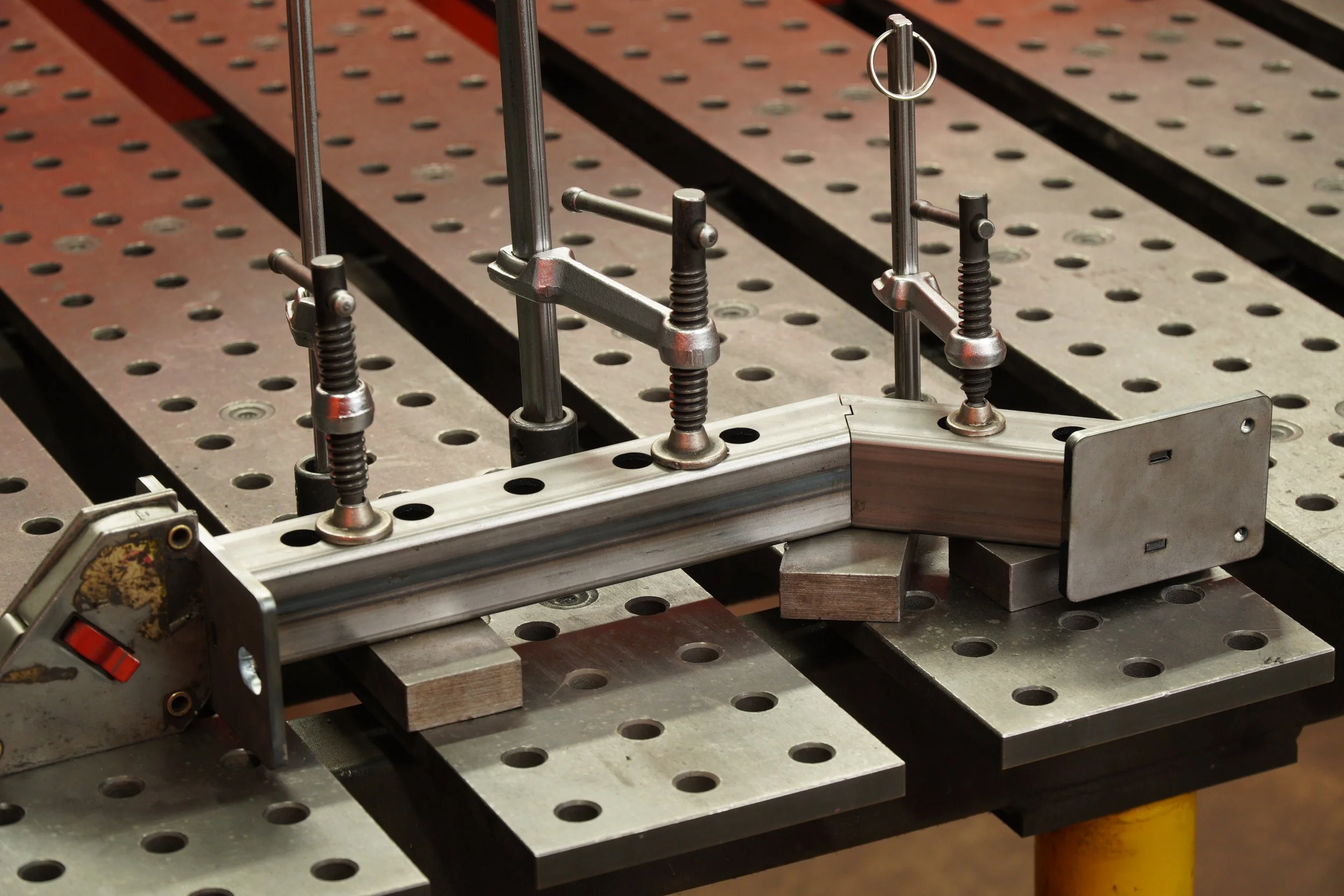 Metal welding fixture clamped to a perforated metal workbench.